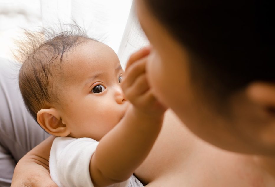 Mother breastfeeding her newborn baby beside window
